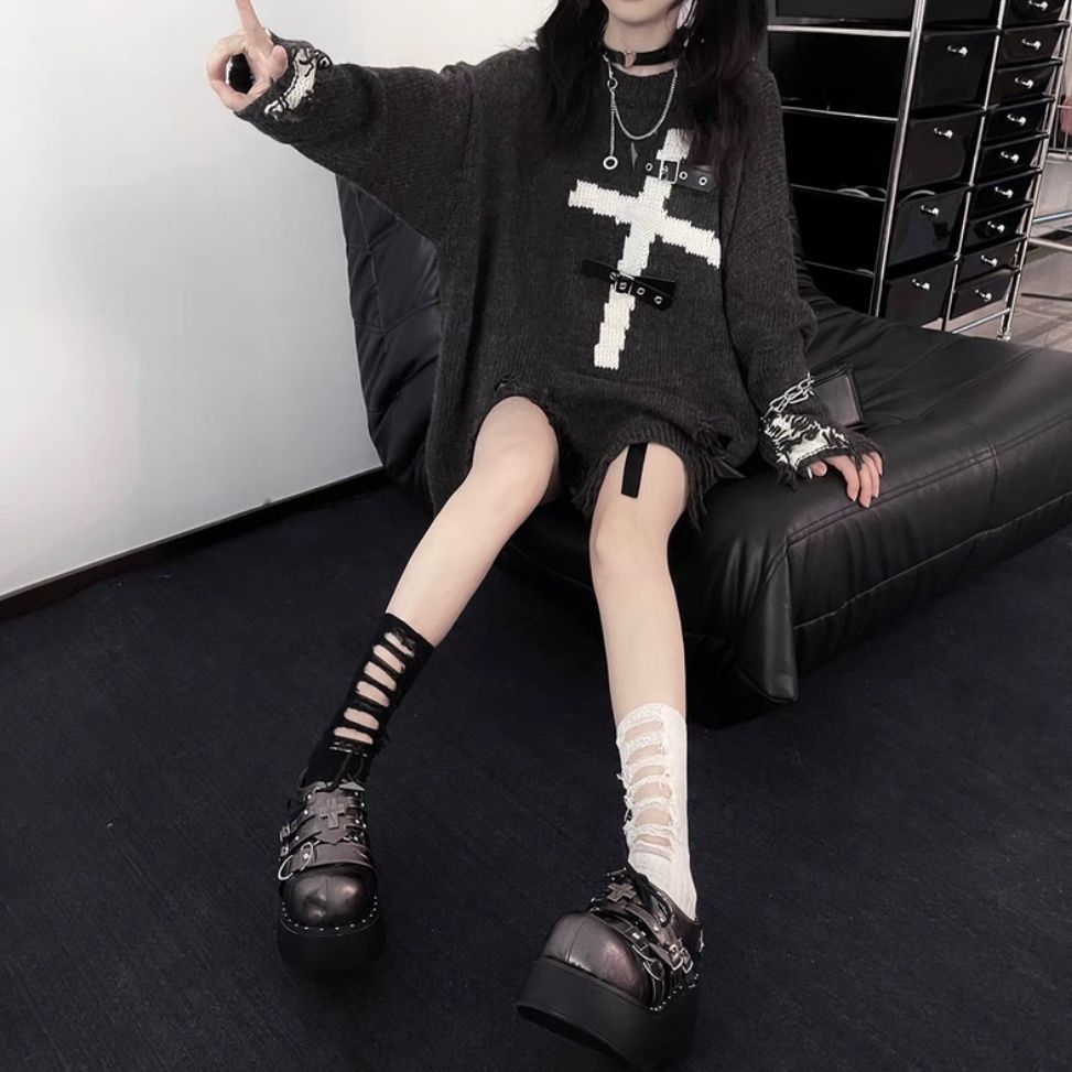 Person sitting on a black couch, wearing an edgy yet comfortable Maramalive™ Dark Cross Loose Sweater - Comfortable Fit for Women with a white cross design, paired with mismatched knee-high socks and chunky platform shoes, gesturing with their hand.