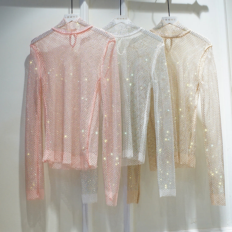 Three Maramalive™ New Crystal Rhinestone Hollow Top Starry Bright Sexy Ladies Long Sleeve See-through Net Diamond Shirts in pink, white, and beige with high collars are hanging on a clothing rack in a store display.