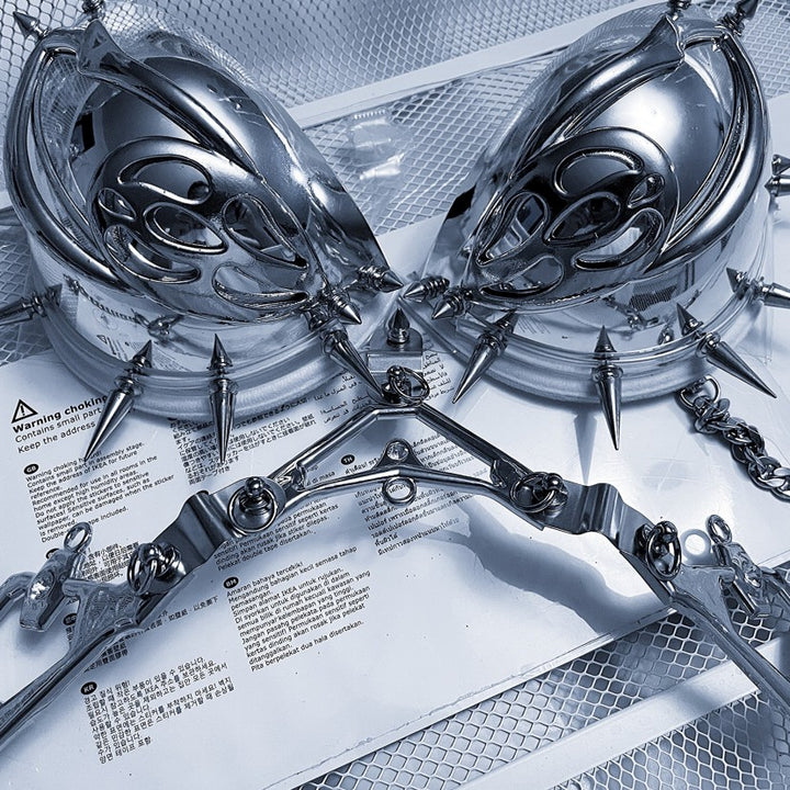 A Punk Futuristic Silver Metallic Performance Suit from Maramalive™ is displayed on a mesh surface, reminiscent of electroplated jewelry, with texts and warnings partially visible underneath.