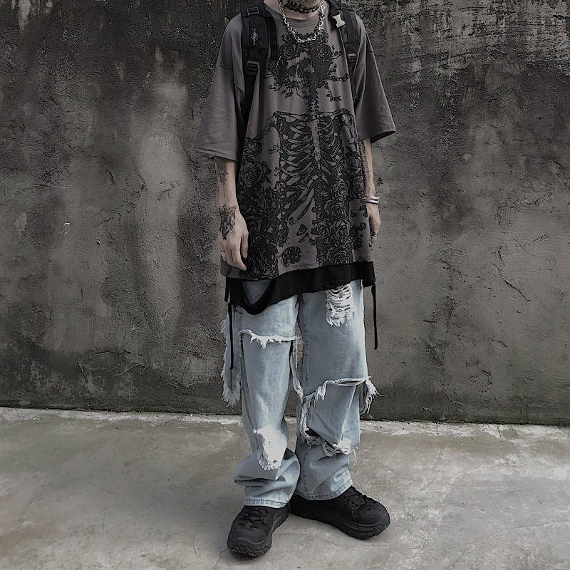 A person dressed in an oversized, graphic print Dark Hip Hop Tee - Perfect for Underground Rap Fans by Maramalive™ and heavily distressed jeans stands against a textured gray wall, wearing black shoes and carrying a backpack. This streetwear fashion look embodies casual cool with an urban edge.