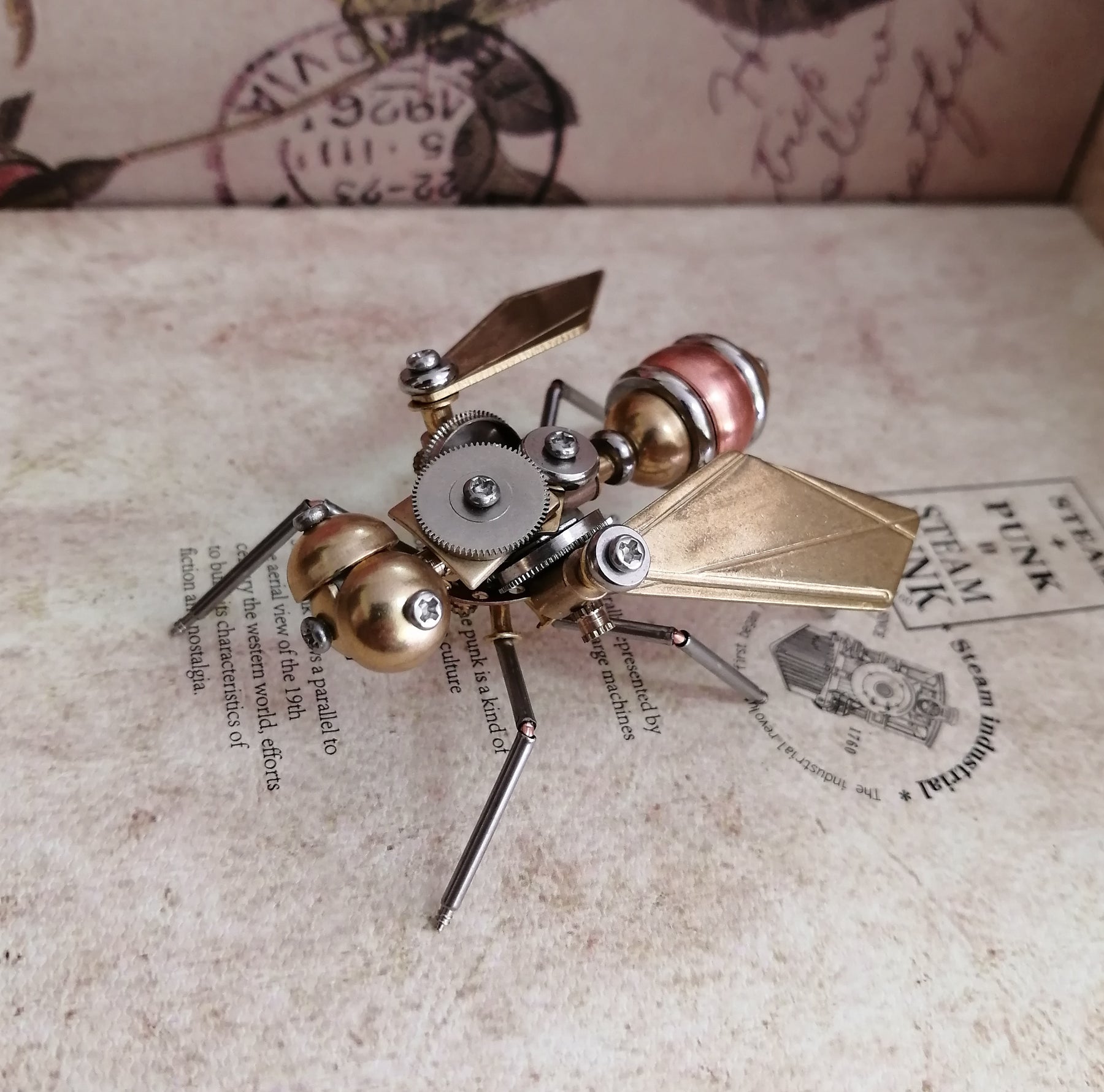 A Maramalive™ steampunk metal fly crafts sitting on top of a book.