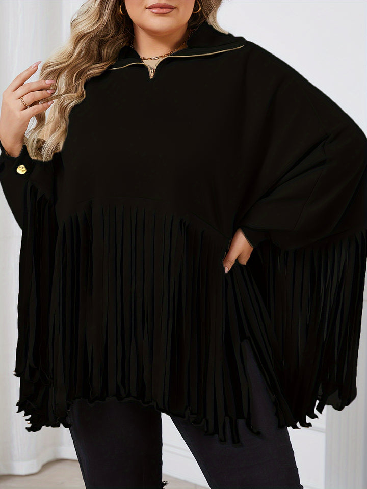 A person wearing a black Maramalive™ Plus Size Trendy Top, Women's Plus Solid Batwing Sleeve Mock Neck Fringe Trim Cloak Top, with long wavy hair and batwing sleeves, stands indoors.