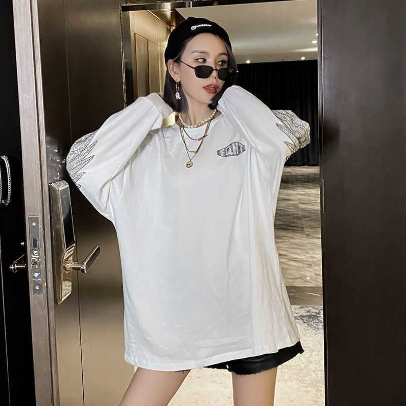 A person wearing a white, Maramalive™ Hot Diamond Mid-Length T-Shirt Women Long Sleeves with a round neck, black shorts, and sunglasses adjusts their hair in an indoor setting.