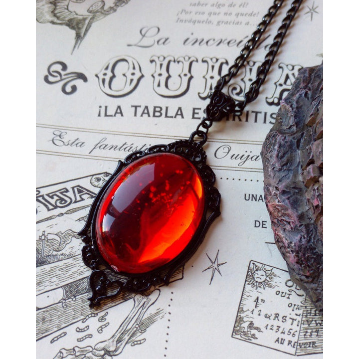 Two Witching Hour necklaces with red and purple stones arranged on an old book for a Halloween vibe by Maramalive™.
