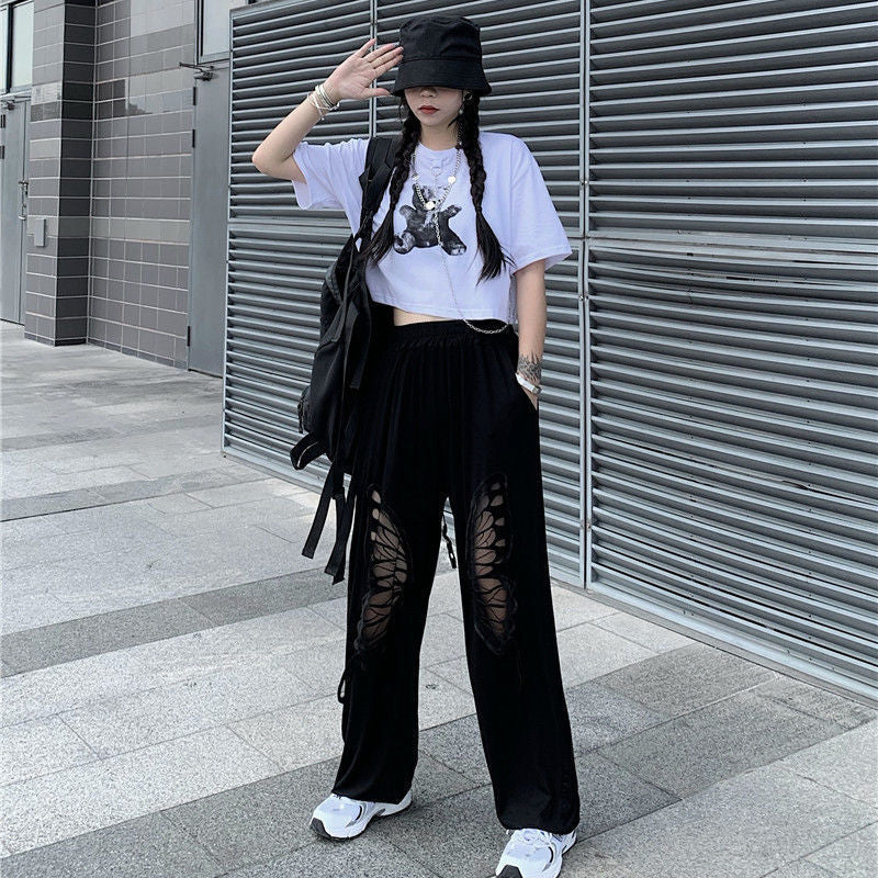 A woman making a bold statement in Unique Baggy Trousers with Cut-outs and Fun Style! by Maramalive™ and a white t-shirt and black pants with a unique patterned Harlem vibe.