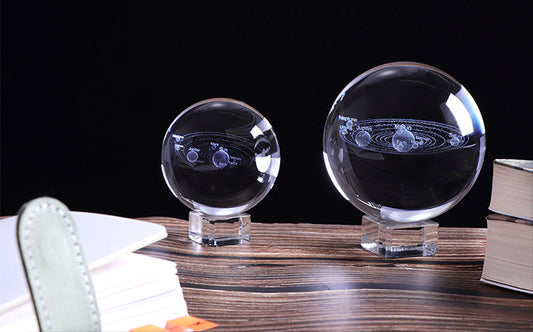 Two Solar System Crystal Balls by Maramalive™ on a table next to a book.