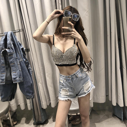 A woman poses in front of a mirror wearing a Maramalive™ Gypsophila shining studded waistcoat strapless tube top strap, ripped denim shorts, and large sunglasses, with a cotton denim jacket hanging on a rack beside her.