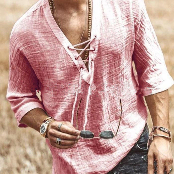 A person wearing a pink, loose-fitting, Maramalive™ Men's Fashion Chest tie Mid Sleeve T Shirt Shirt with five-point sleeves and various accessories, including bracelets and a necklace, holds a pair of sunglasses outdoors. The background appears to be a field.