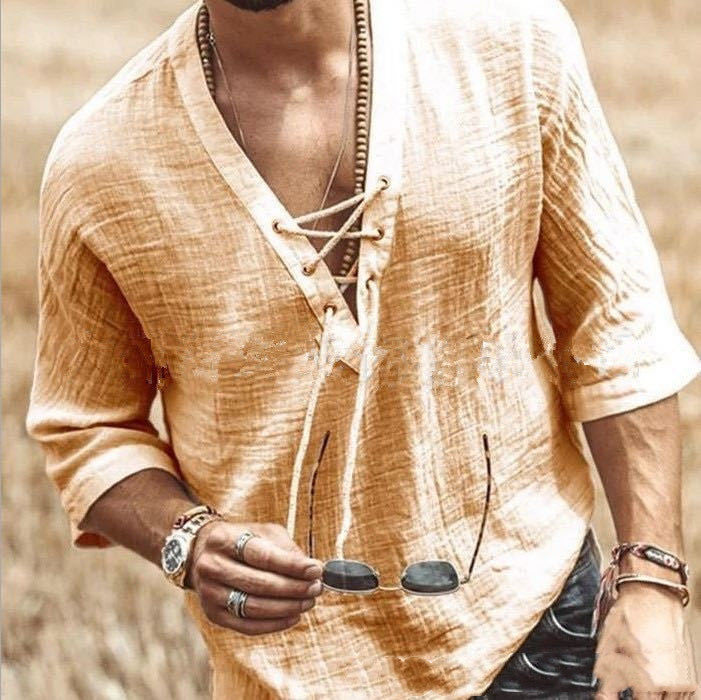A person wearing a loose-fitting, beige, Maramalive™ Men's Fashion Chest tie Mid Sleeve T Shirt showcases several bracelets and rings while holding sunglasses in their left hand. The background is an out-of-focus outdoor scene.