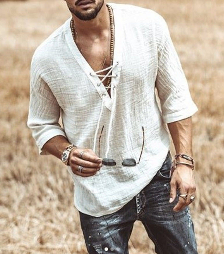 A man wearing a loose-fitting, long-sleeve, lace-up white Maramalive™ Men's Fashion Chest tie Mid Sleeve T Shirt Shirt made of polyester fiber and jeans holds sunglasses in one hand, standing in a grassy field.
