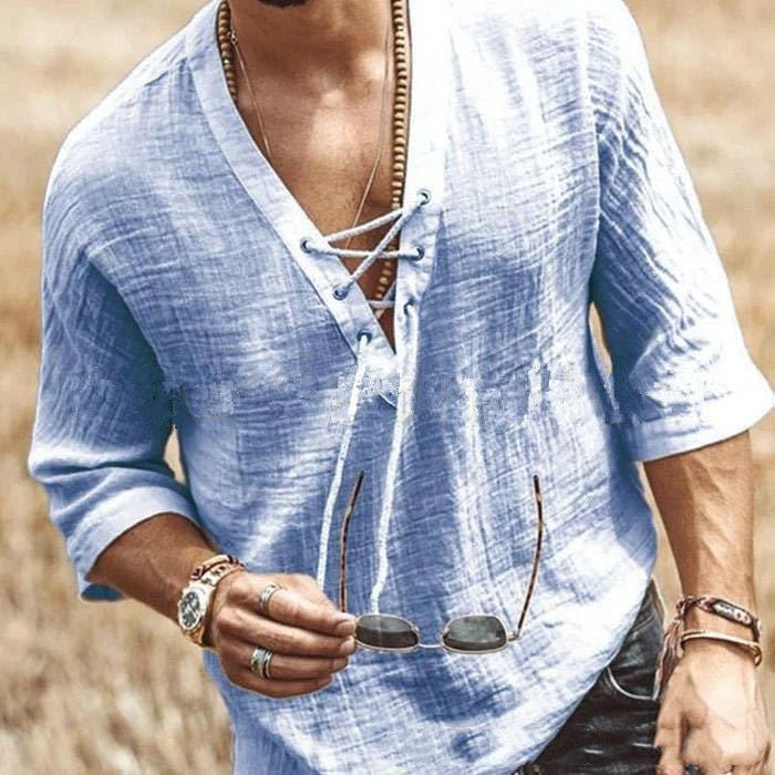 A person wearing a light blue, lace-up shirt with five-point sleeves holds sunglasses in one hand. The individual has several accessories, including rings, bracelets, and a necklace. This loose edition Maramalive™ Men's Fashion Chest tie Mid Sleeve T Shirt made from polyester fiber adds a touch of casual elegance to their style.