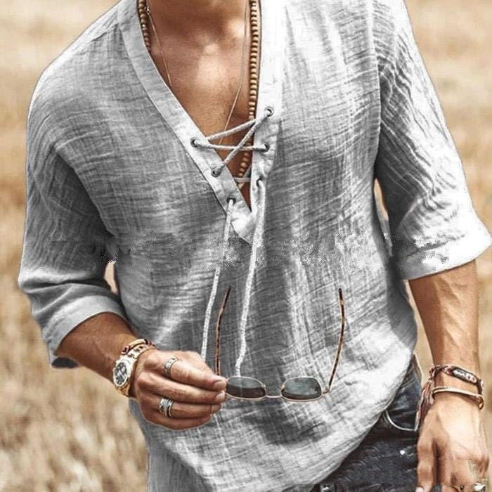 A person wearing a light gray, loose edition, Maramalive™ Men's Fashion Chest tie Mid Sleeve T Shirt holds a pair of sunglasses. The person also wears multiple bracelets and necklaces.