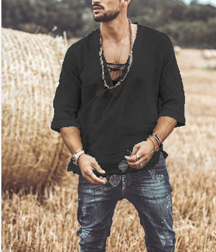 A man stands in a field with hay bales, wearing a Maramalive™ Men's Fashion Chest tie Mid Sleeve T Shirt, paired with blue jeans. He has several necklaces and a wristwatch. The background is blurred vegetation.