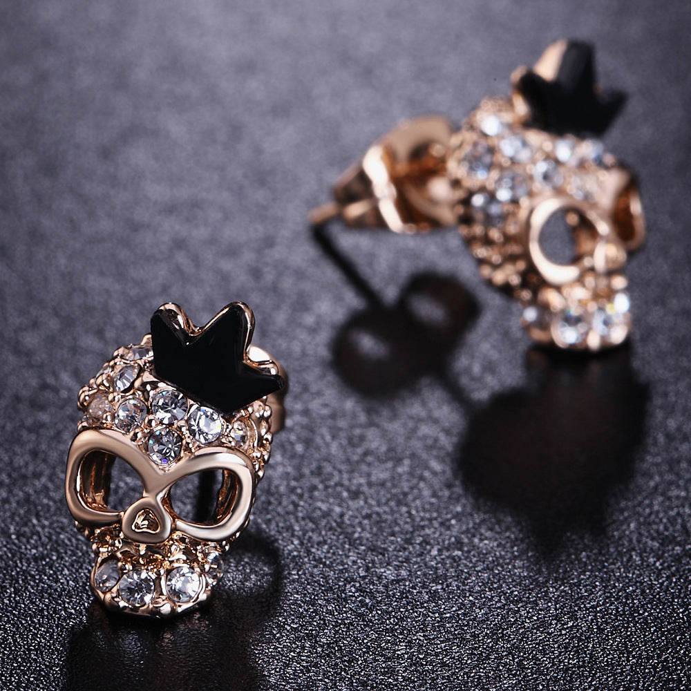 A pair of Maramalive™ gold-plated skull earrings with black diamonds.