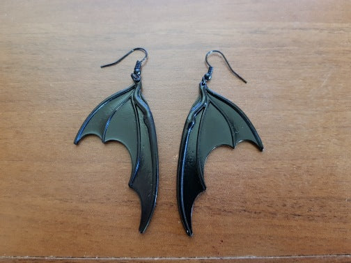 A pair of Vintage Dark Halloween Bat wings Earrings Gothic Earrings Vampire Black Bat Earrings from Maramalive™ on top of an old book.