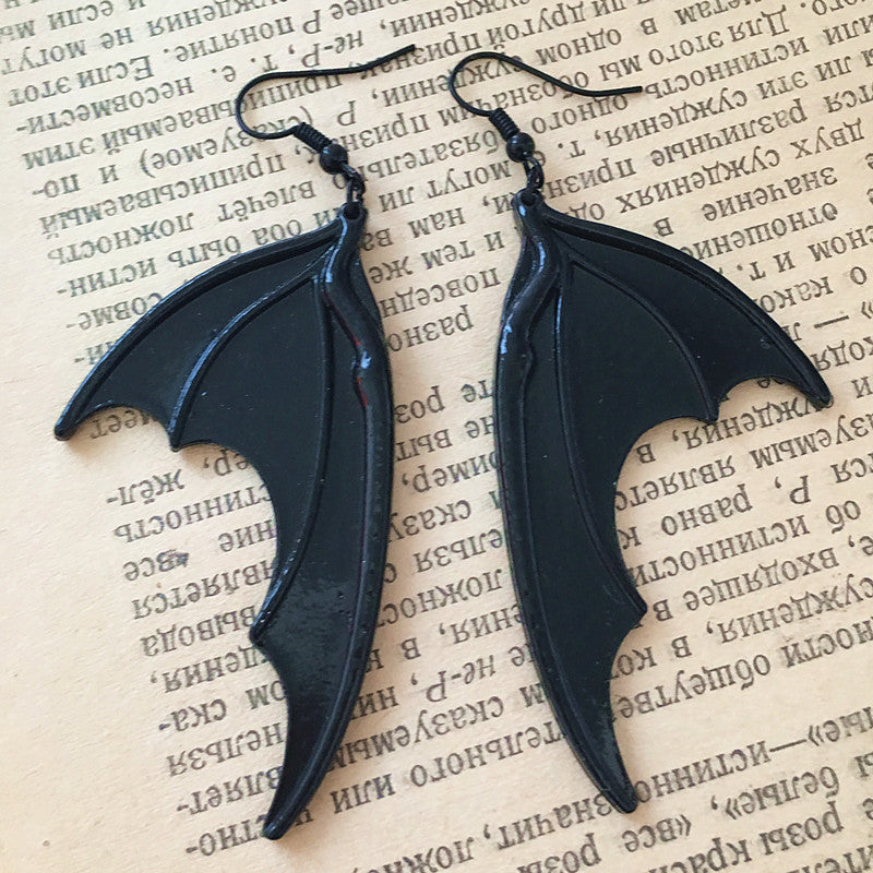 A pair of Vintage Dark Halloween Bat wings Earrings Gothic Earrings Vampire Black Bat Earrings from Maramalive™ on top of an old book.