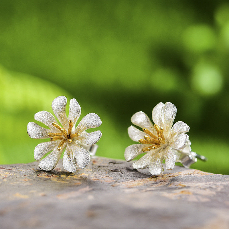 A pair of Maramalive™ Handmade Women's Earrings, silver flower stud earrings, on top of a rock.