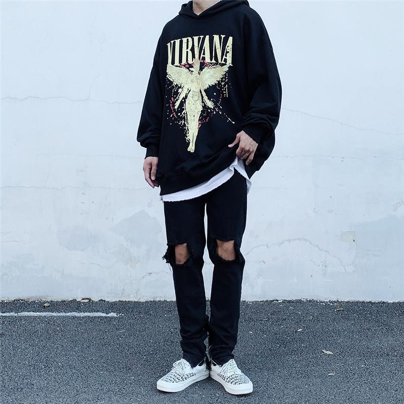 A person wearing an Oversized Punk Style & Hoodie Sweatshirt: Edgy Look by Maramalive™, distressed black jeans, and white sneakers stands against a white wall on a paved surface.