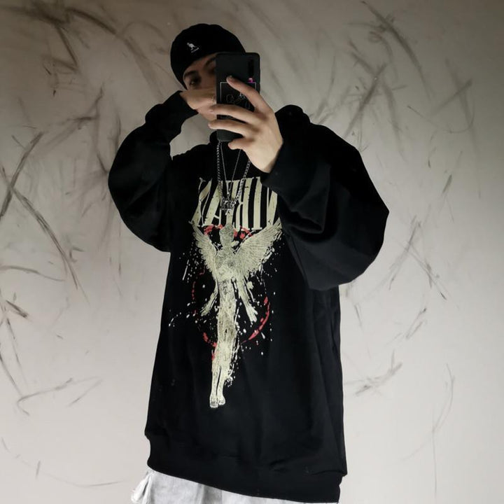 Person taking a mirror selfie wearing an Oversized Punk Style & Hoodie Sweatshirt: Edgy Look by Maramalive™ with a gothic fallen angel graphic, a black beanie, and necklaces. The background has abstract, dark smudges on a light wall.