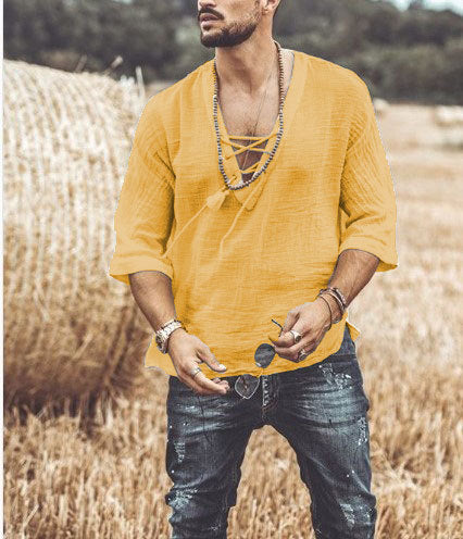 Man in a yellow loose edition Maramalive™ Men's Fashion Chest tie Mid Sleeve T Shirt with lace-up detail and five-point sleeves, standing in a field with hay bales. He’s wearing jeans and accessorized with necklaces, bracelets, and sunglasses made from durable polyester fiber.
