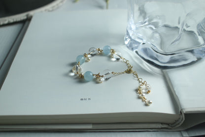 A book with a Clear Quartz Aquamarine Bracelet from Maramalive™ on it next to a glass of water.