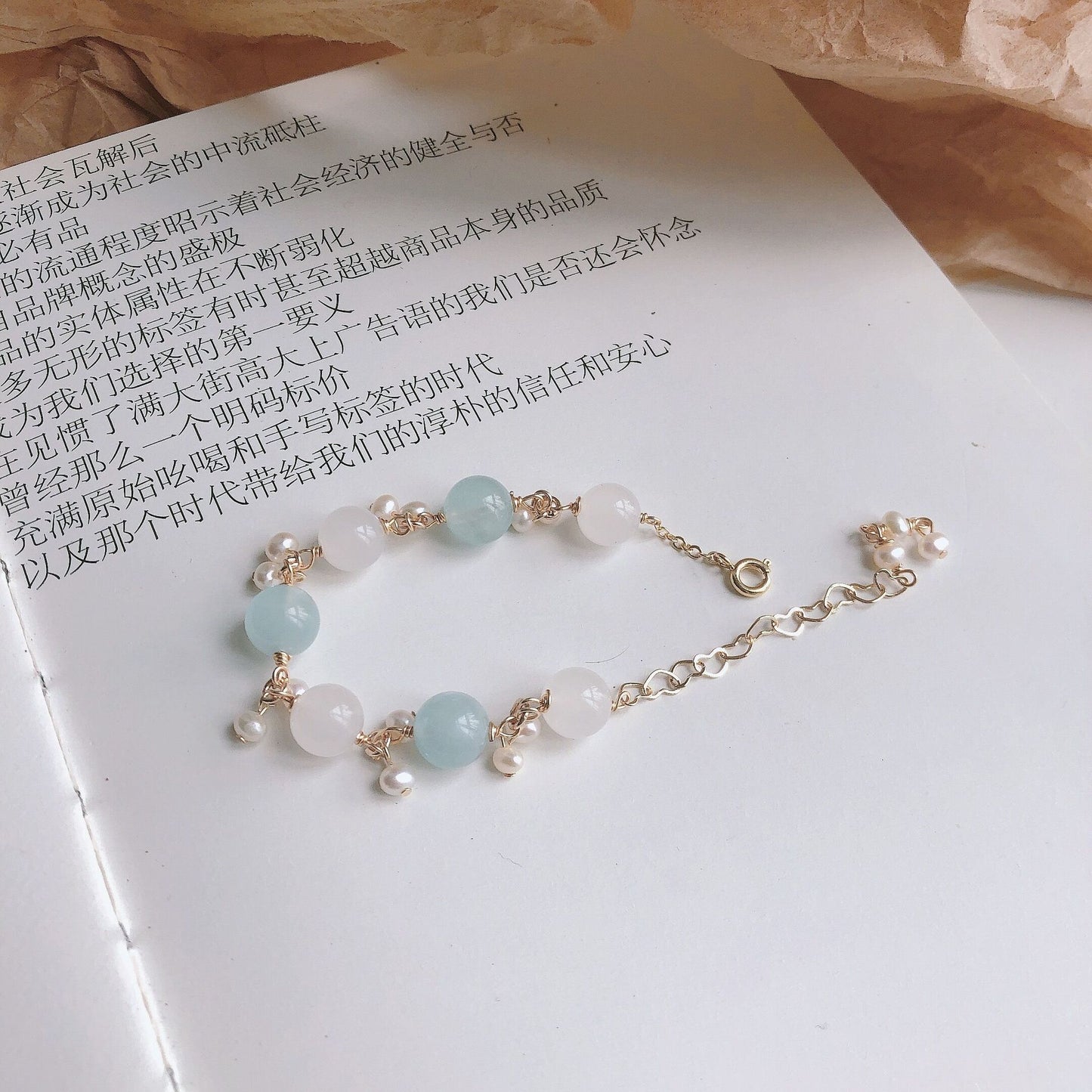 A book with a Clear Quartz Aquamarine Bracelet from Maramalive™ on it next to a glass of water.