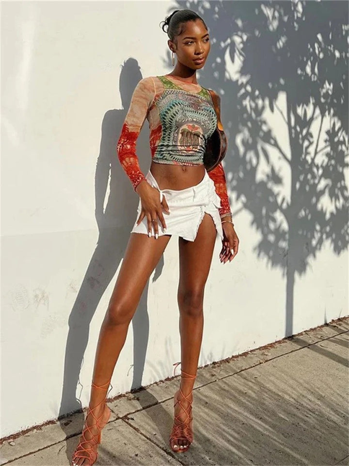 A woman stands against a wall in dappled sunlight, embodying European and American style with a Maramalive™ Fashion Digital Printing Colorful Breathable Women's Round Neck Pullover, white cut-off shorts, and strappy high heels.