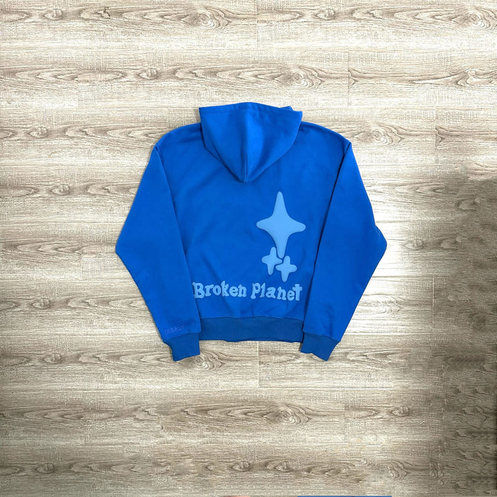 A blue polyester Maramalive™ Letter Foam Printed Hoodie Punk Rock Casual Sweater with a graphic of a stylized star and the text "Broken Planet" on the back, laid flat on a wooden floor – perfect for the street hipster aesthetic.