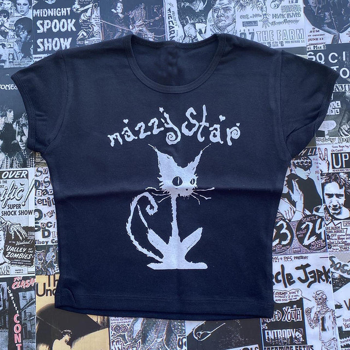 A black Maramalive™ Gothic Street T-shirt Women's Printed Black Top with a white stylized cat graphic, featuring a slim fit, is displayed on a background covered in various punk rock posters and flyers.