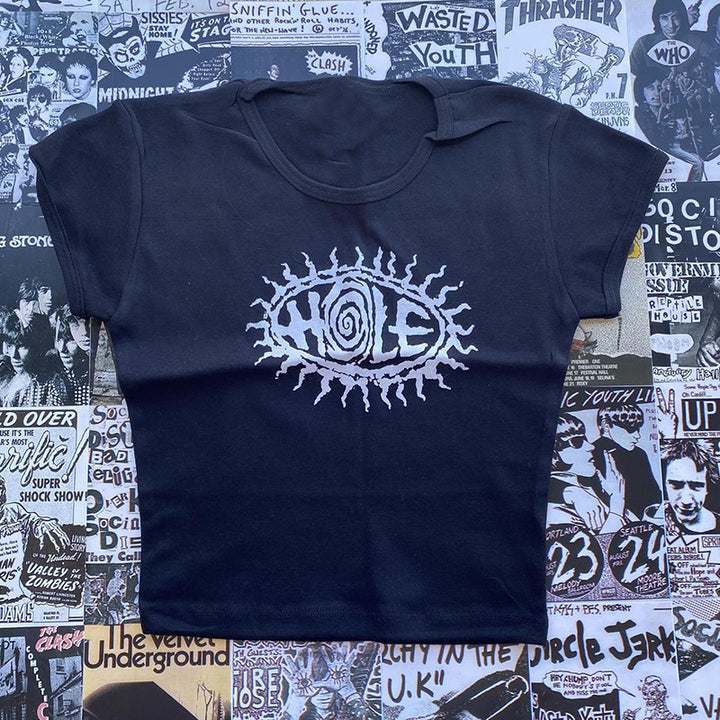 A Maramalive™ Gothic Street T-shirt Women's Printed Black Top with the word "HOLE" printed in the center, surrounded by a geometric pattern of abstract shapes. The background is a collage of various punk rock posters and album covers.