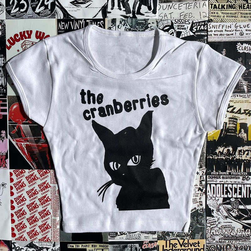 A Maramalive™ Gothic Street T-shirt Women's Printed Black Top with a black cat graphic and the text "the cranberries" printed on it, laid on a surface covered with various band posters and ads, features a subtle Gothic style woven into its design.