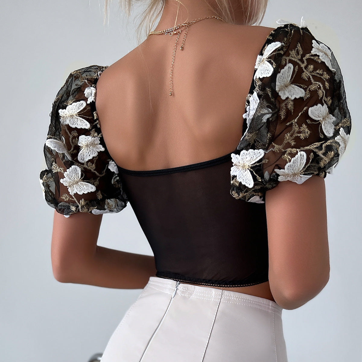 A person is shown from behind wearing a Maramalive™ Ladies New Hot Girl Backless See-through Camisole with puff sleeves featuring white floral embroidery, embodying European and American style, paired with white high-waisted pants.