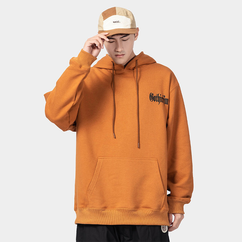 A person wearing an orange Maramalive™ European Hip Hop Gothic Sweater Men's Hoodie with a dimensional patch pocket and a color-blocked cap stands with their head slightly down, touching the brim of the cap.