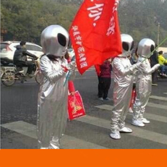 Three individuals dressed in Maramalive™ Alien show costume Suits holding a red flag stand at a street crossing, looking like they're ready for a sci-fi convention.