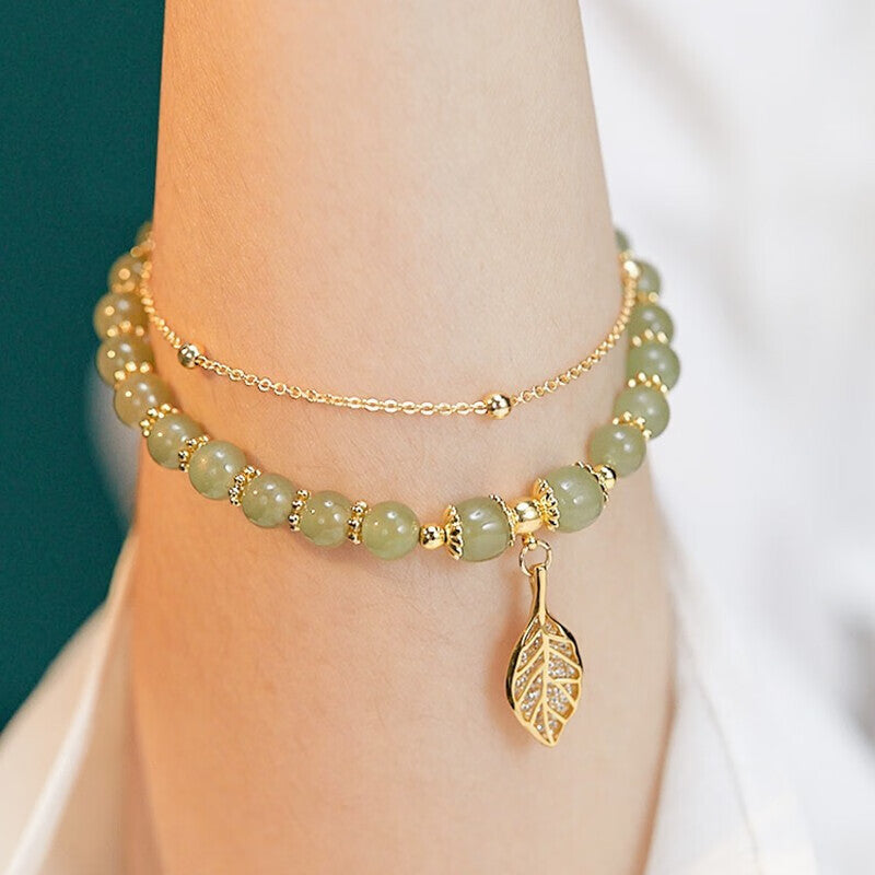 A woman wearing a Maramalive™ S925 Sterling Silver Descendants Of The Rich Hetian Jade Bracelet with a leaf and gold charm.