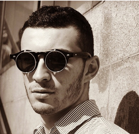 A man wearing Black Retro SteamPunk Sunglasses by Maramalive™ in front of a wall.