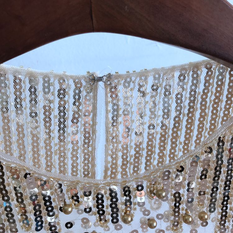 Close-up of a women's Fashion Bottoming Shirt Sequined Top For Women made with beige polyester fiber and shiny sequins in a striped pattern, hanging on a wooden hanger. The garment, by Maramalive™, is designed as free size.