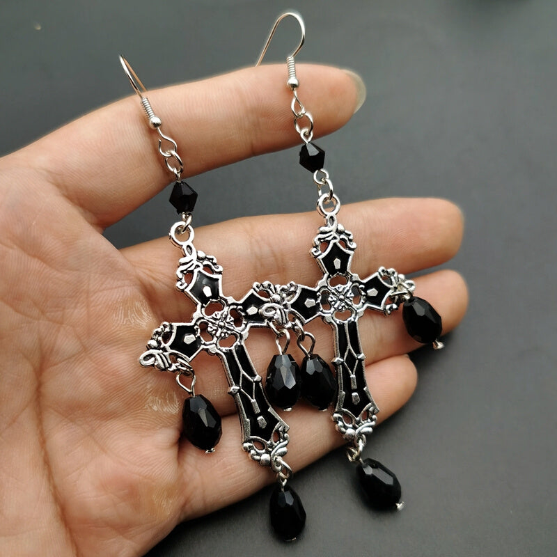 A pair of Gothic Black Cross Garnet And Crystal Chandelier Earrings La hanging from a person's hand, from the brand Maramalive™.