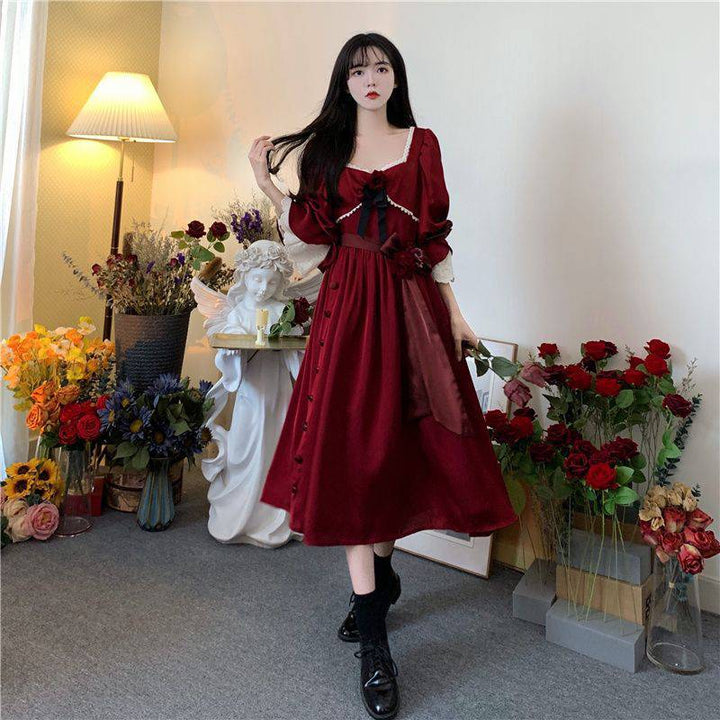 A woman in a Maramalive™ Velveteen Gothic Red-Rose Dress: Vintage Wine-Red Frock standing in front of flowers.