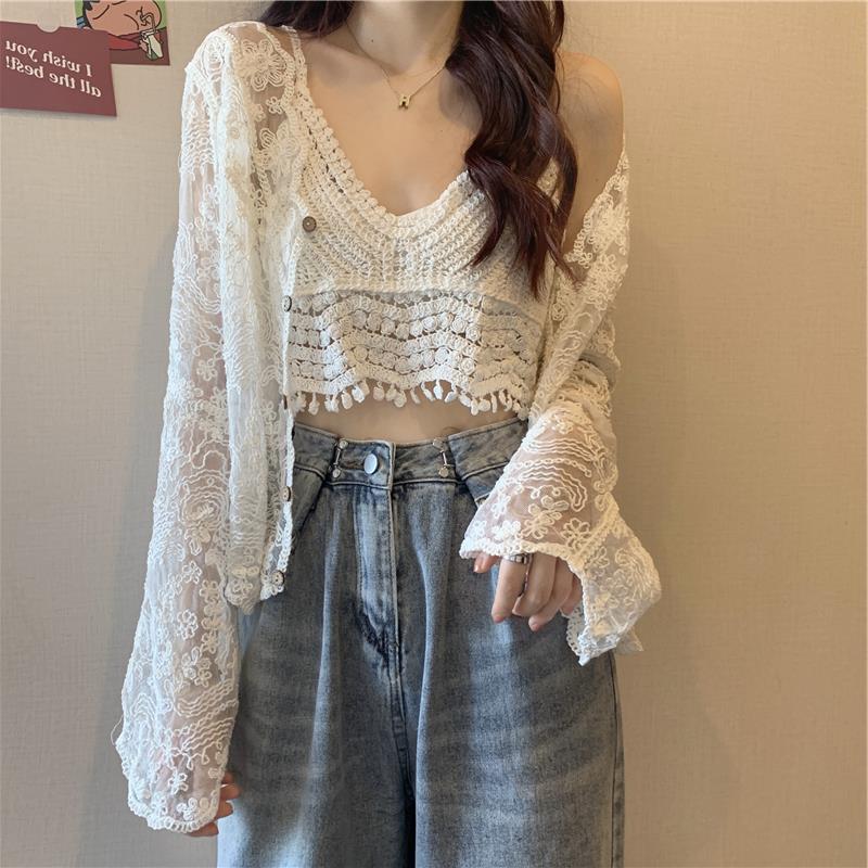 A person wearing a Maramalive™ Crocheted Two-piece Set Female Summer New Western Style Blouse Top with crocheted flowers and high-waisted blue jeans stands in front of a beige wall.