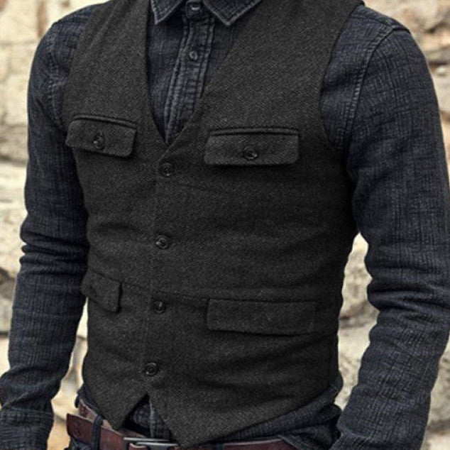 A person wearing a dark-colored, British-style button-up shirt and a charcoal gray vest with pockets stands in front of a stone wall. The European And American Men's Vest Casual Solid Color Herringbone Vest by Maramalive™, available in sizes XS to XXXL, boasts a classic yet modern appeal perfect for any occasion.