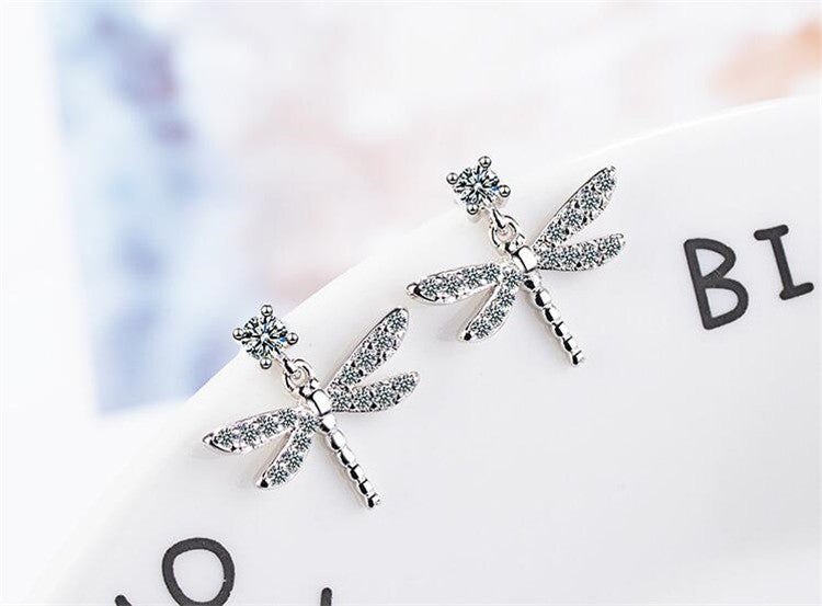 A pair of Maramalive™ Women's Dragonfly Diamond Earrings on a white plate.