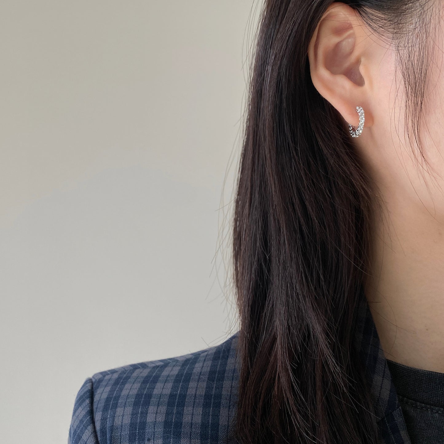 A woman wearing a plaid jacket is touching her Maramalive™ S925 Sterling Silver Round Ear Clip Diamond.
