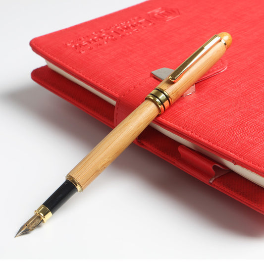 A red notebook with a Maramalive™ Natural Bamboo Fountain Pen Sign Pen sitting on top of it.