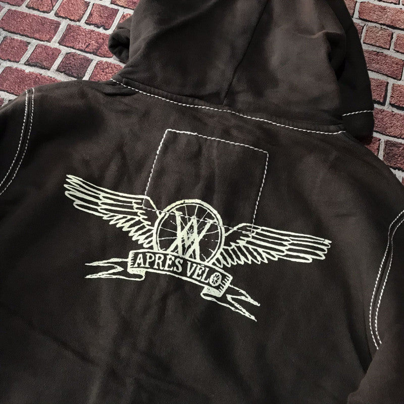 Back view of a loose fit brown Maramalive™ Hooded Sweater Motorcycle Heavy Metal Punk Can Take Lovers with a stitched design featuring a winged emblem and the text "APRÈS VÉLO" on a brick-patterned background.