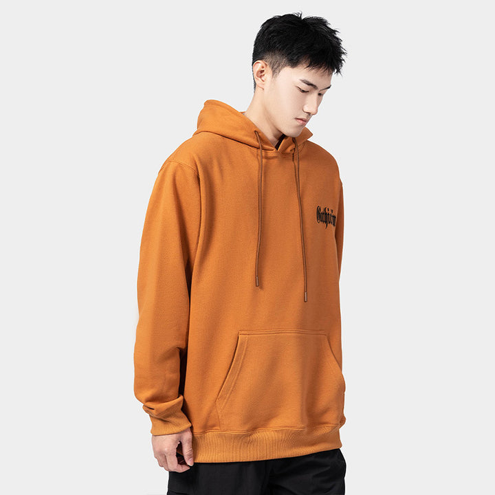 A person stands against a plain background, wearing an orange Maramalive™ European Hip Hop Gothic Sweater Men's Hoodie with a dimensional patch pocket and black pants, looking slightly down to the side.