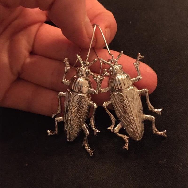 A pair of Gothic Alloy Cockroach Insect Earrings Europe And America by Maramalive™ in a person's hand.