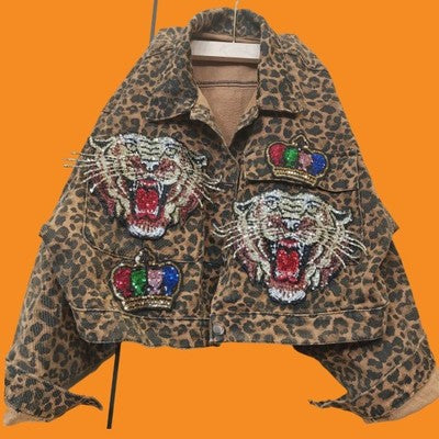 A Leopard Print Studded With Nails Bead Mesh Gauze Stitching Denim Short Coat Female featuring embellished roaring tiger faces and multicolored crown patches on both front sides. Made with durable triacetate fiber, this statement piece from Maramalive™ comes in various size options. The image background is a solid orange color.