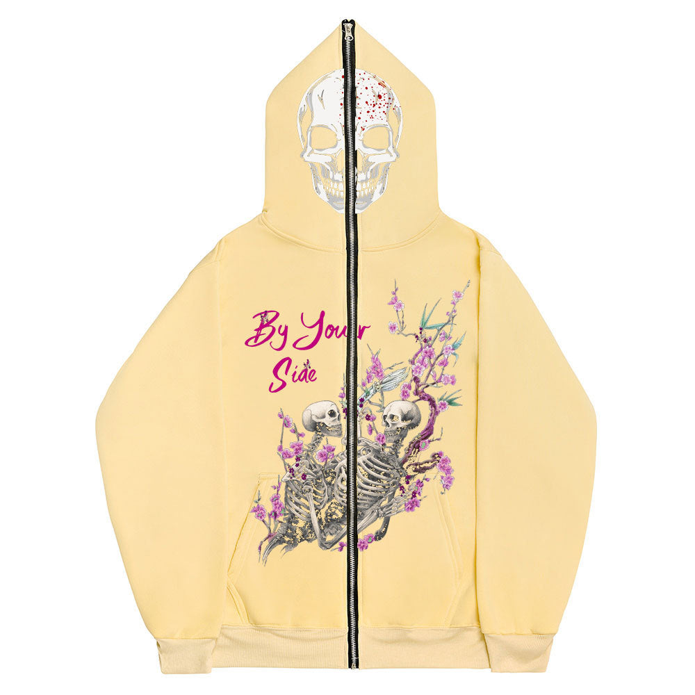 A light yellow Gothic Zipper Sweater: The Perfect Gothic Top Multi-colors by Maramalive™ with a skull print on the hood and two skeletons surrounded by pink flowers on the front, along with the text "By Your Side.