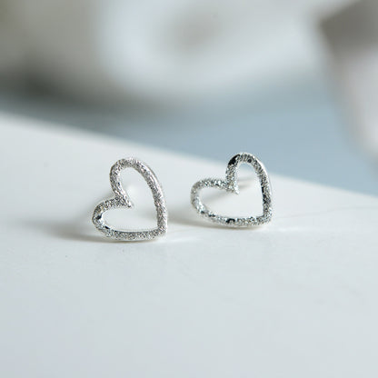 A pair of Maramalive™ S925 Sterling Silver Earrings Hollow Frosted Heart-shaped Ear Studs on top of a book.